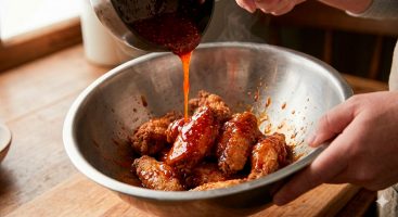 Mezclando alitas de pollo horneadas con salsa Sriracha y miel en bol grande