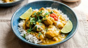 The final plating and presentation. The final image shows the finished dish. The chicken curry, with its creamy golden sauce, is served over a bed of fluffy basmati rice. It is garnished with abundant freshly chopped cilantro and a lime slice, ready to be enjoyed. The silky consistency of the sauce is evident.